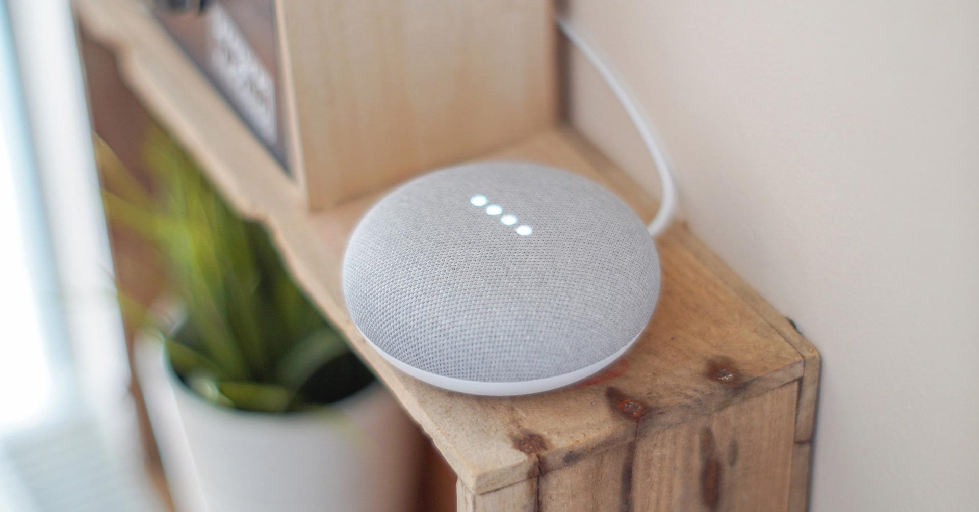 A smart assistant speaker, developed Google, sitting on a bookshelf.