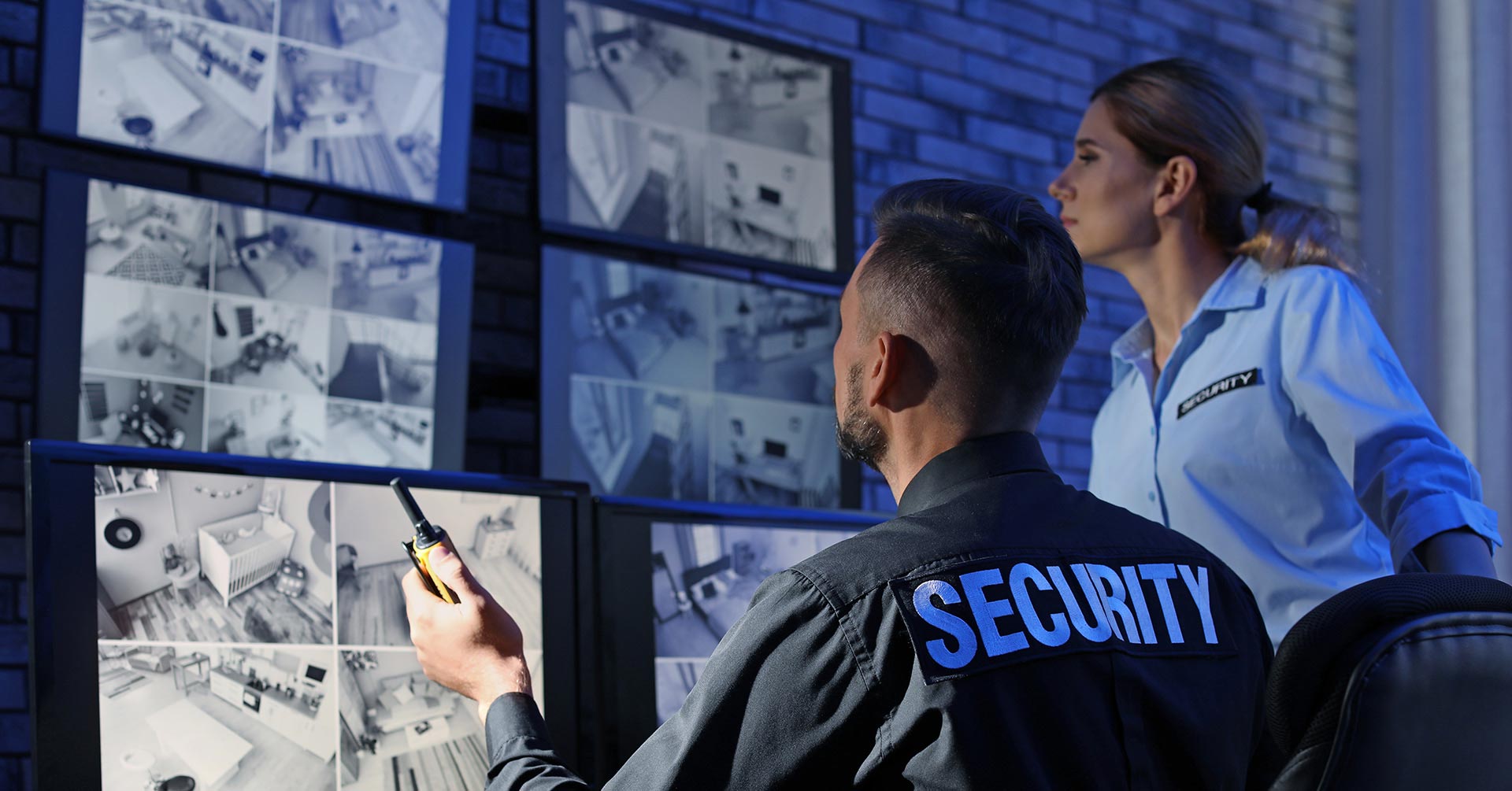 Two security guards viewing secutity footage on multiple monitors 