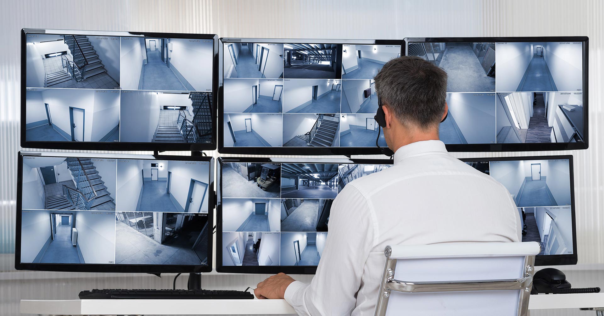 A security guard sitting in front of multiple monitors, observing live CCTV footage.