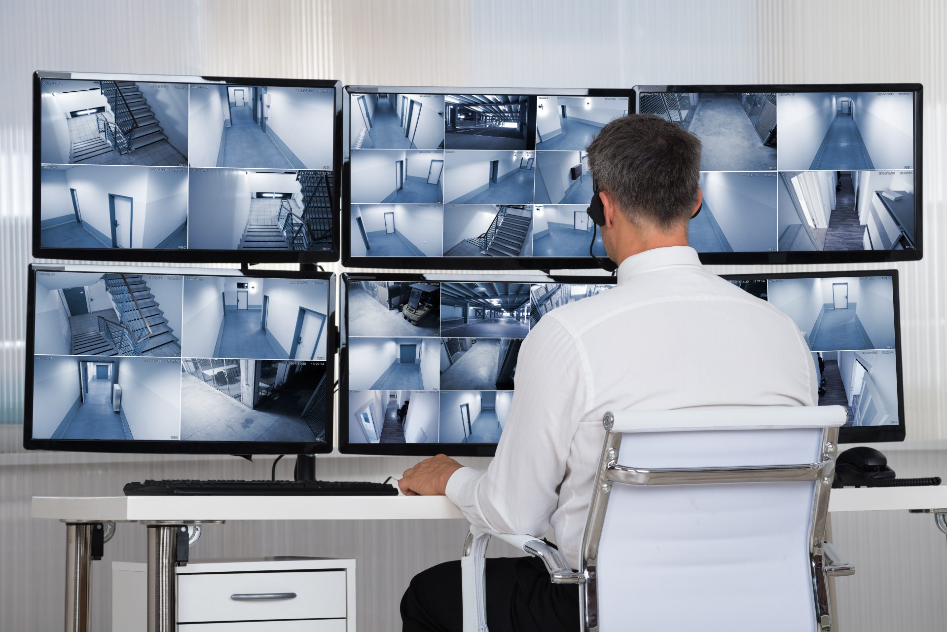 A security officer sitting at a desk with multiple CCTV monitors 