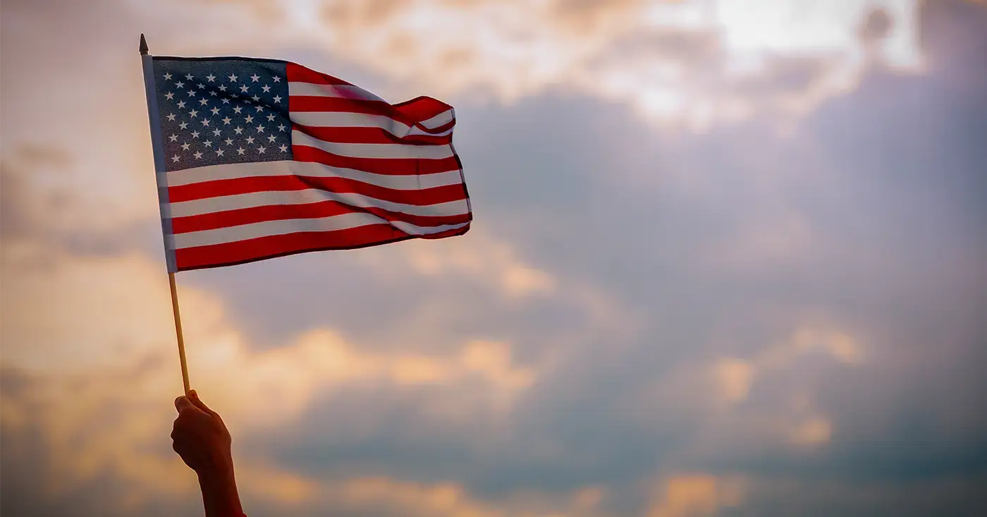 American flag waving at sunset, symbolizing America250 celebrations and the need for heightened vigilance around major public events.