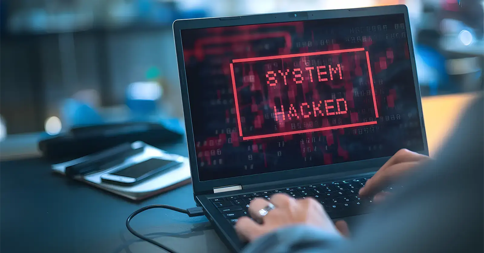 Cybercrime system hacked: Person using laptop with a system hacked message displayed