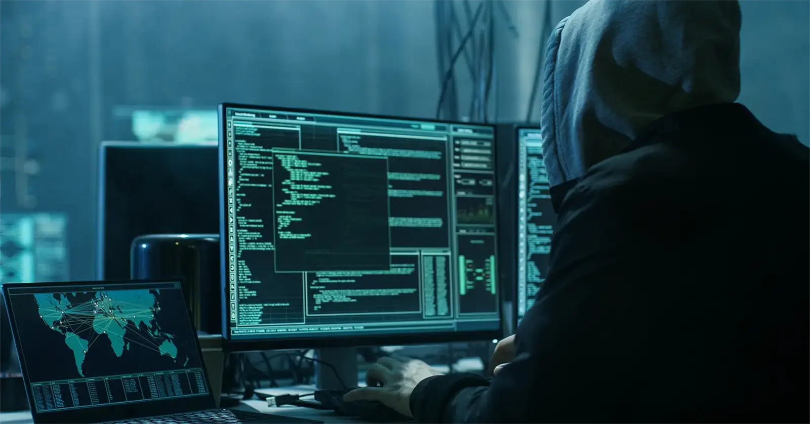 Hooded figure sitting at a laptop searching the dark web