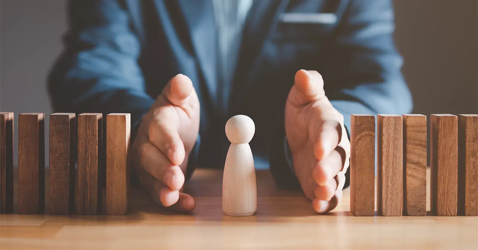 Hands surrounding wooden figure from falling dominos. Risk management and assessment concept. Person protecting their employees from risk. 