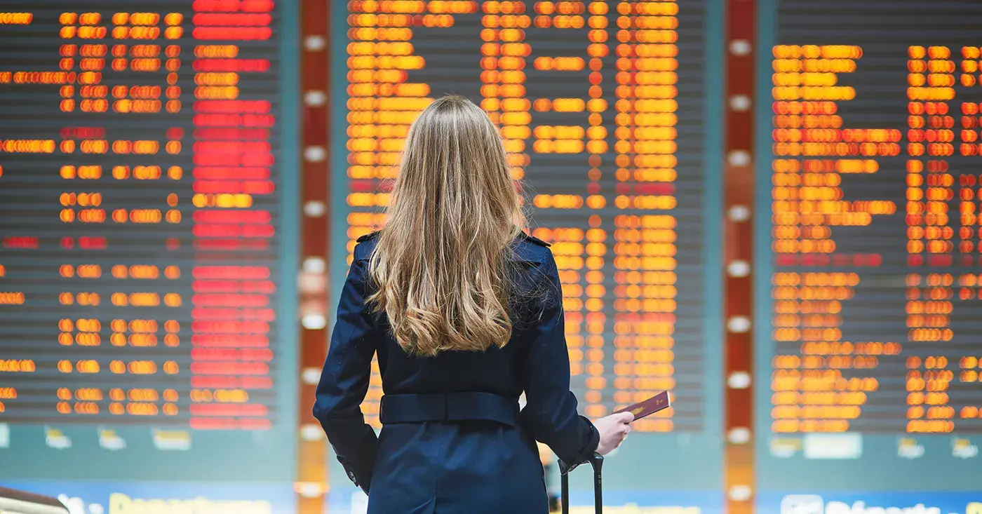 A corporate traveller viewing a flight board full of delays and cancellations in an airport.