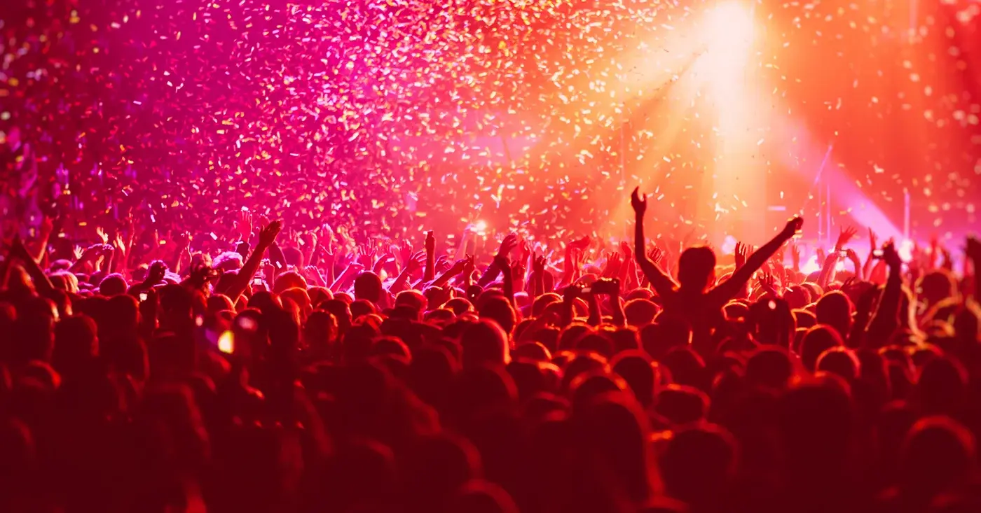 Large concert crowd under red stage lights and falling confetti, highlighting the scale and complexity of security at major live events.
