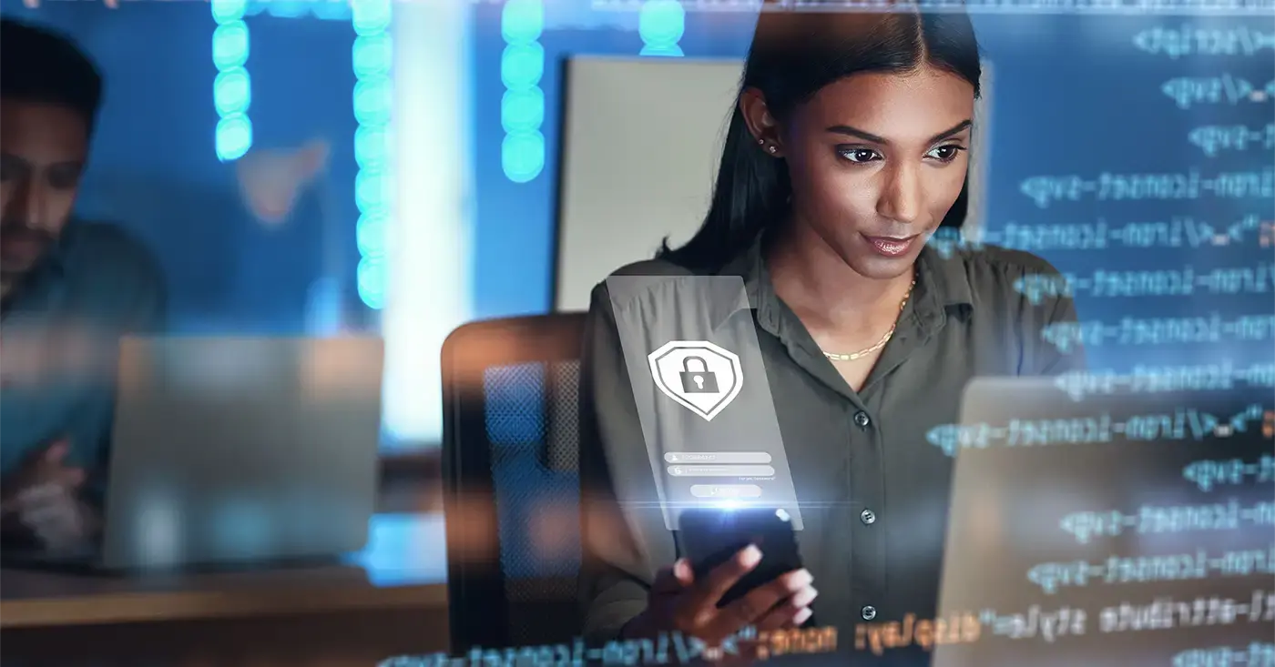 Cybersecurity analyst using AI-powered threat detection tools on a laptop and smartphone to proactively prevent security risks in a corporate environment.