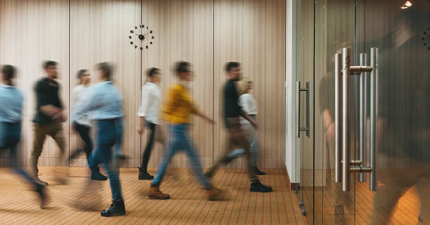 Blurred office workers walking through a hallway, representing everyday employees and the often-overlooked risks of workplace violence beyond executive protection