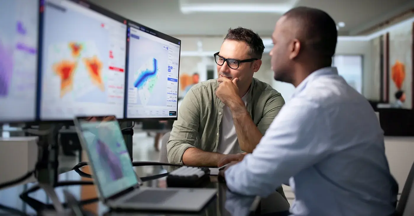 Two analysts reviewing maps and risk data across multiple monitors, illustrating how GSOC teams assess threat patterns and escalation.