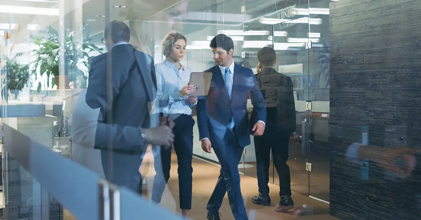 Business professionals reviewing security information on a tablet in a modern office corridor.