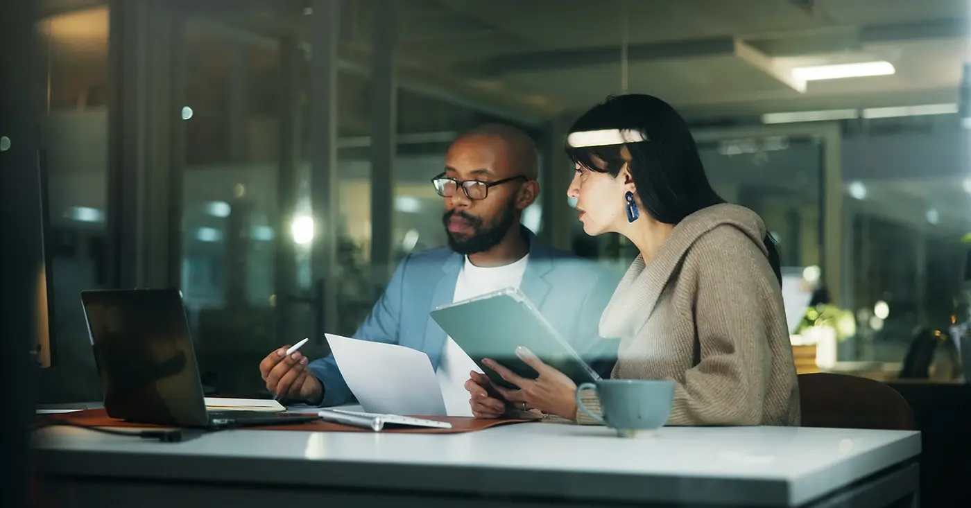 Two professionals reviewing documents and data on a laptop, representing cross-functional collaboration in proactive workplace violence prevention programs