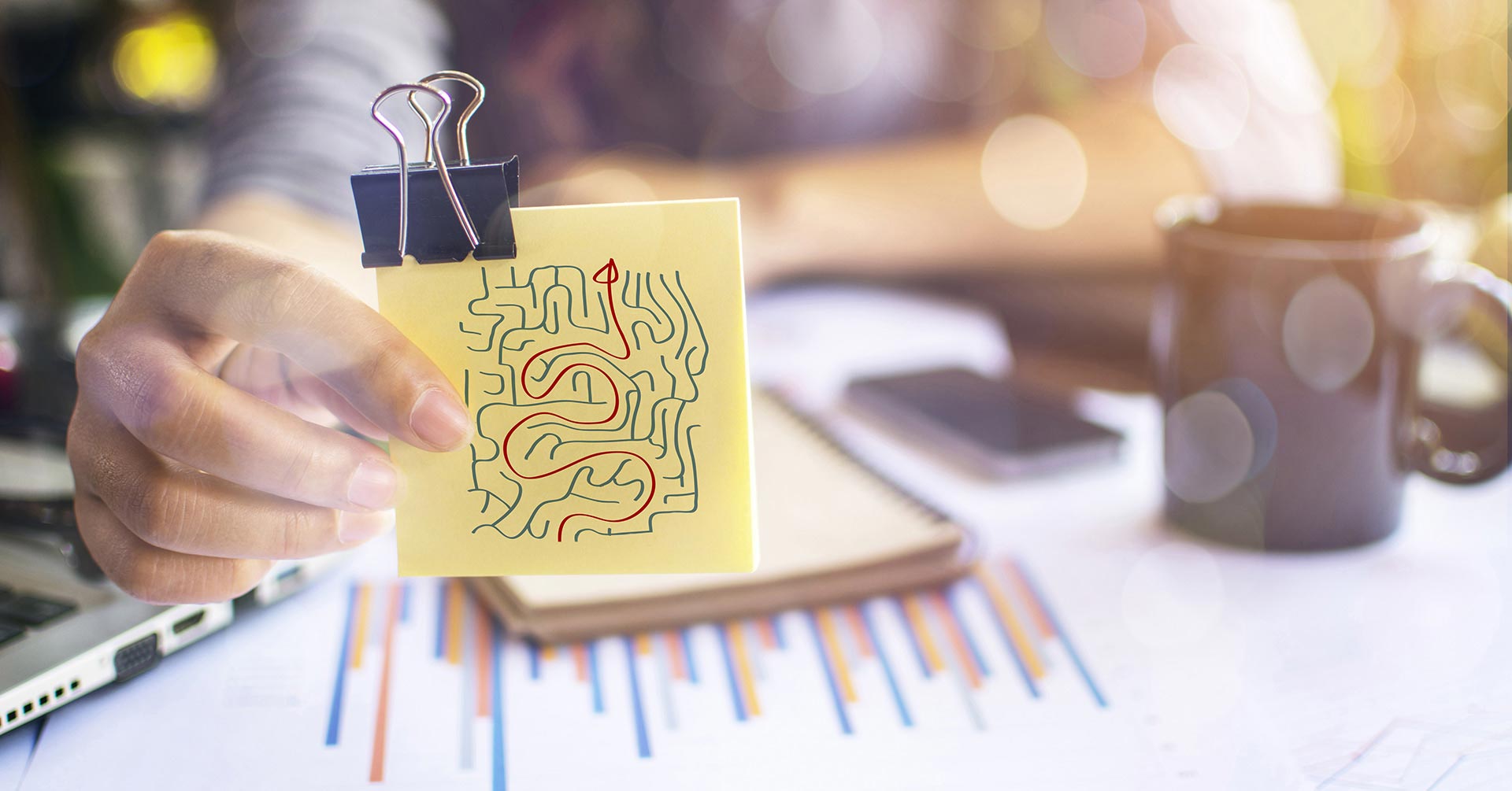 A woman holding a post-it note of a maze with the solution to the puzzle highlighted in red ink